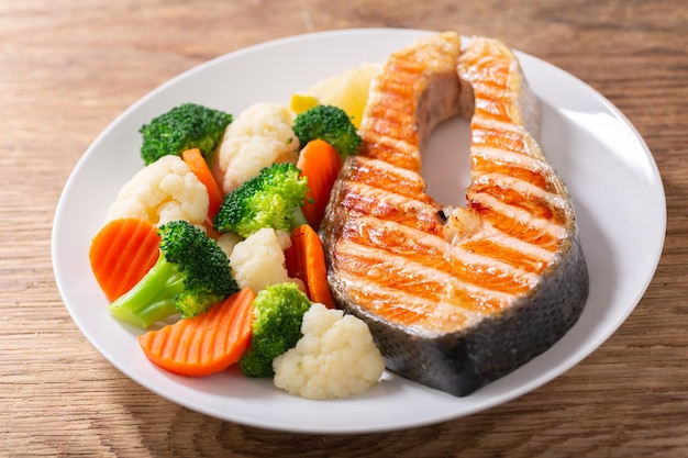 plate of grilled salmon steak with vegetables on wooden table