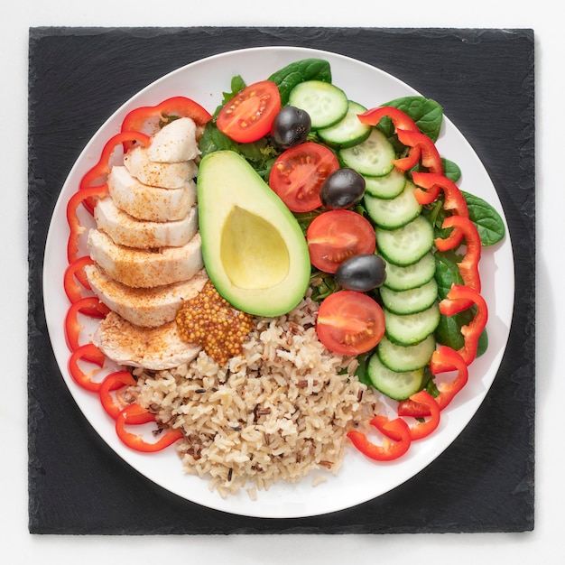 Plate of healthy food Chicken fillet, salad, avocado, and whole grain rice porridge. In a white plate on a stand of black slate.