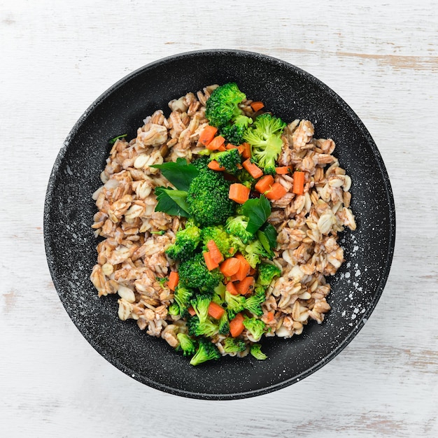 A plate of healthy food Oatmeal with broccoli carrots and parsley Top view On a white wooden background Free copy space