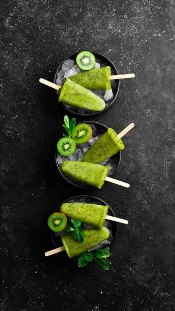 A plate of Homemade popsicles with kiwi On a black stone background
