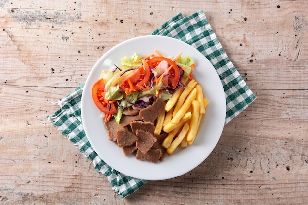 Plate of kebab, vegetables and french fries on wooden table