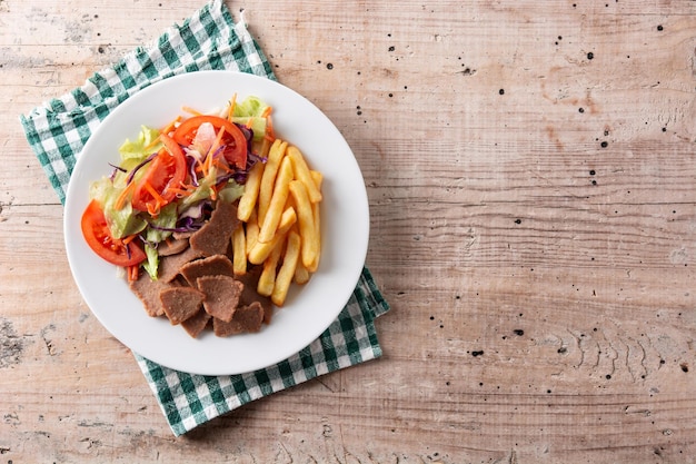 Plate of kebab, vegetables and french fries on wooden table