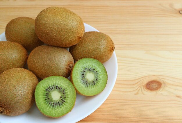 Plate of many fresh ripe whole fruits and crosssections of kiwi fruits on wooden table