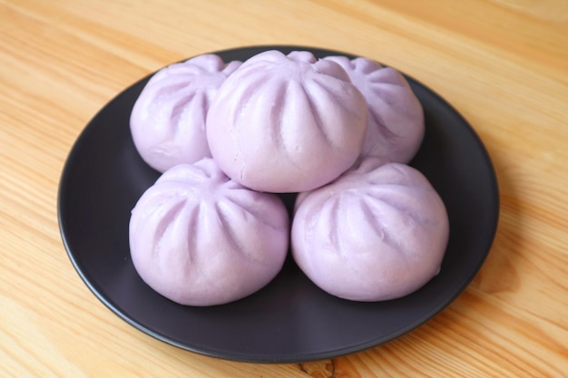 Plate of many purple sweet potato steamed buns served on wooden table