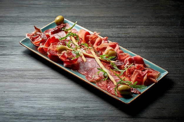 Plate of meat antipasti with salami, jamon in a blue plate on a wooden background