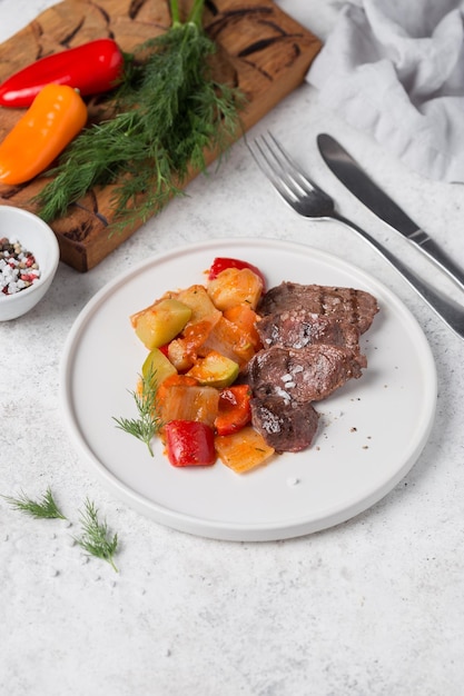 A plate of meat with vegetables and a knife on a table with a fork.