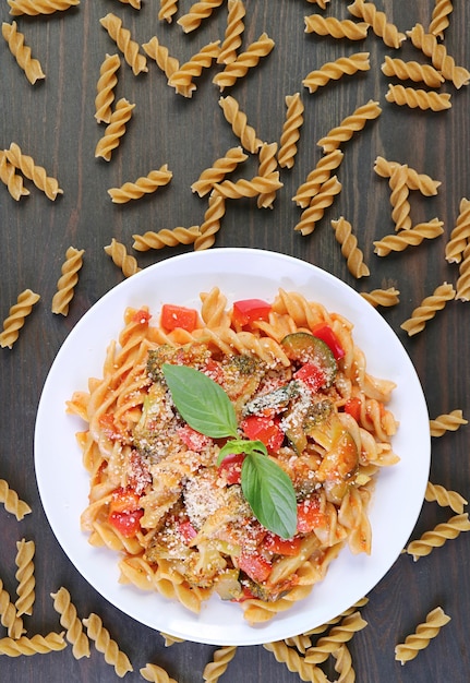 Plate of mouthwatering whole wheat fusilli pasta in tomato sauce with dried pasta scattered around