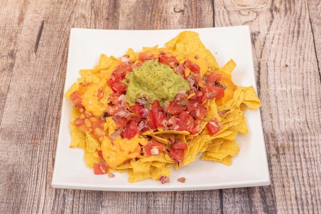 Plate of nachos with guacamole cheddar cheese chopped tomato and onion with beans in sauce