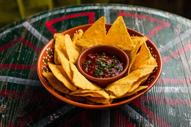 A plate of nachos with spicy salsa dip on a wooden table