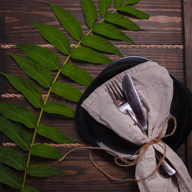 A plate and a napkin with a fork on it and a leaf on the table.