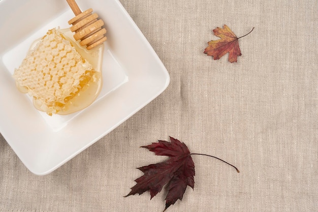 写真 テーブルの上の新鮮な蜂蜜の櫛のプレートは、天然のリネンナプキンの上面図の落ちた紅葉を提供しました