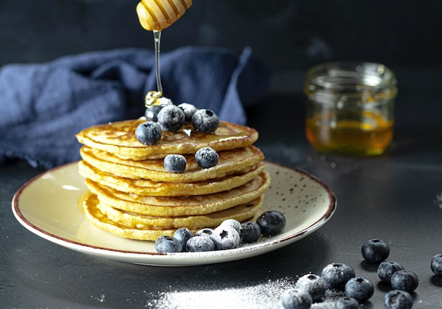 Plate of pancakes topped with blueberries and honey