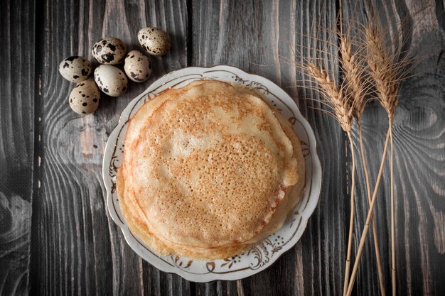 A plate of pancakes with quail eggs and a spica on a wood table.