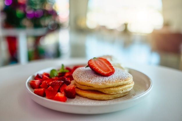 A plate of pancakes with strawberries and whipped cream serving on the table