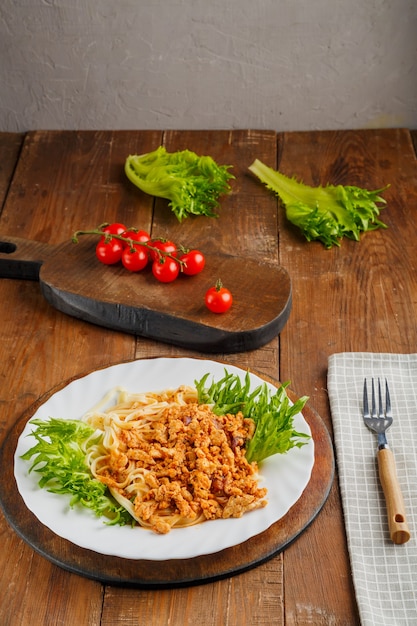 A plate of pasta in bolognese sauce on a nearby fork and cherry tomatoes on a board. Vertical photo