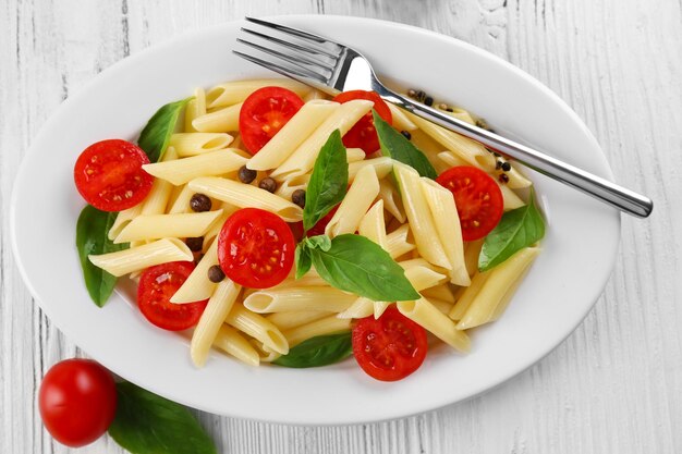 Plate of pasta with cherry tomatoes and basil leaves on table closeup