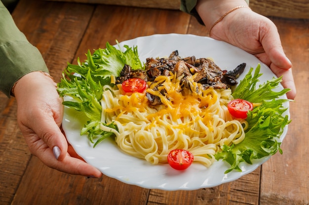 A plate of pasta with mushrooms and cheese decorated with herbs in female hands. Horizontal photo