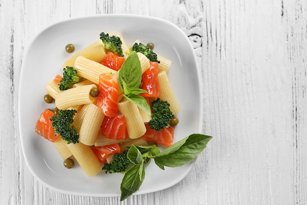 Plate of pasta with salmon and broccoli on wooden table top view