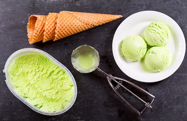 Plate of pistachio ice cream scoops and waffle cones on dark , top view