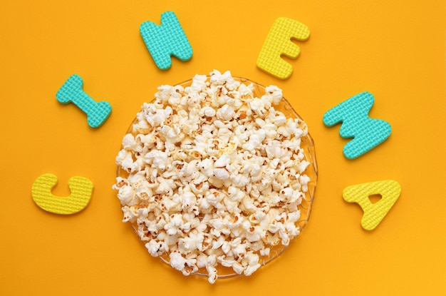 A plate of popcorn on a yellow background and inscription cinema