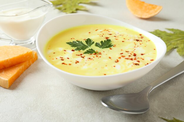 Plate of pumpkin soup and ingredients on white textured table