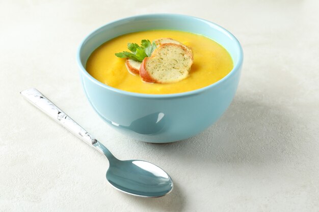 Plate of pumpkin soup and spoon on white textured table
