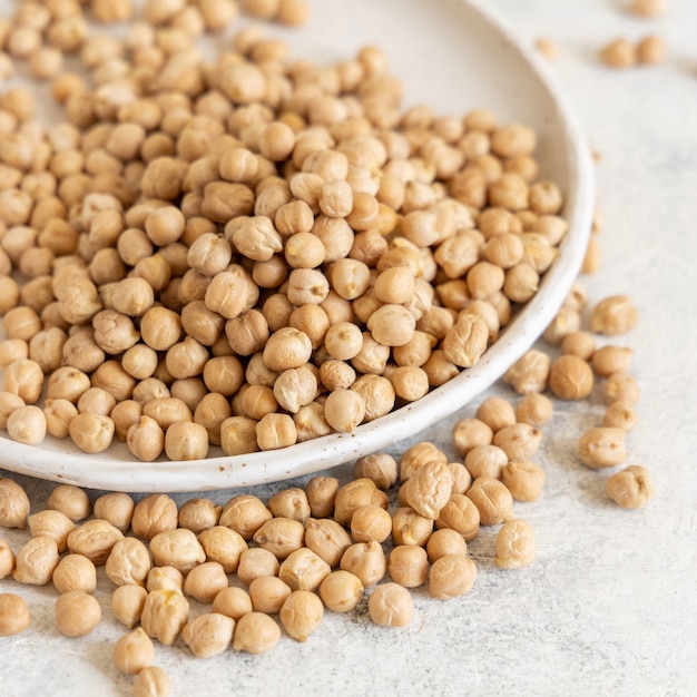 Plate of raw dry chickpea on white table close up