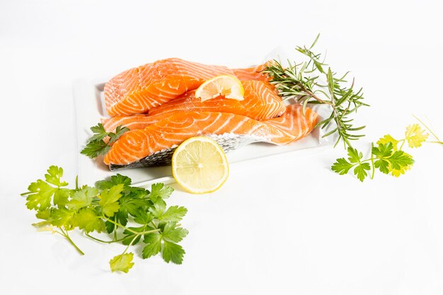 Plate of raw and fresh salmon fillets with herbs, parsley and lemon on a white background