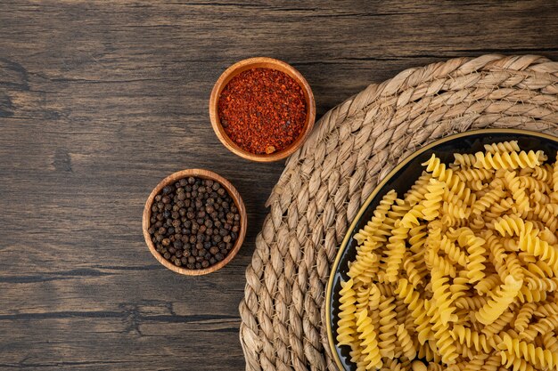 Plate of raw fusilli, condiments and raw eggs on wooden surface. 