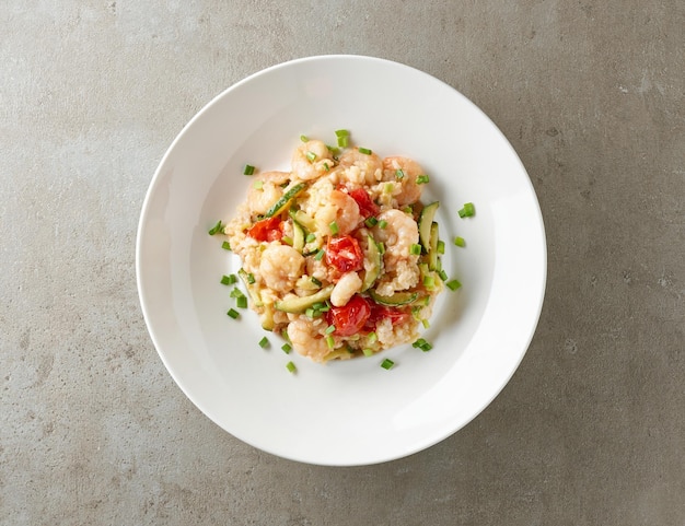 Plate of risotto with zucchini and prawns on grey restaurant table top view