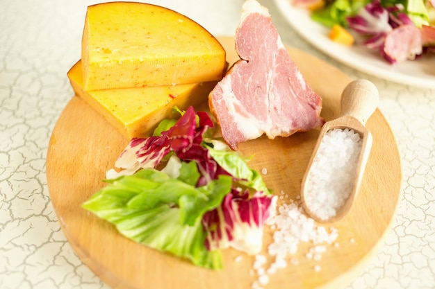 A plate of salad of green leaves, ham and cheese. Plate of salad with green leaves, ham and cheese. Fresh lettuce, cheese, ham and sea salt on a cutting board. Intercontinental breakfast at the hotel.