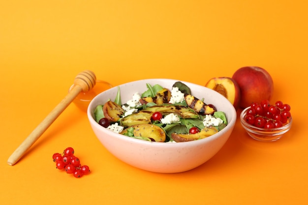 Plate of salad with grilled peach on orange background