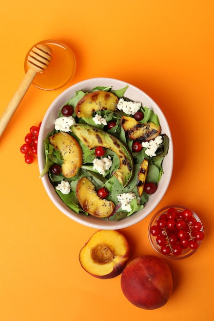 Plate of salad with grilled peach on orange background