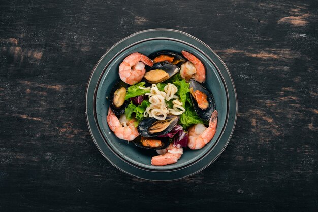 A plate of seafood Mussels squid shrimp Top view On a black wooden background Copy space