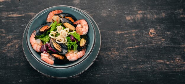 A plate of seafood Mussels squid shrimp Top view On a black wooden background Copy space