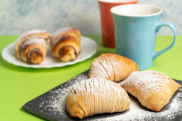 A plate of sfogliatelle and croissants with a cup of coffee next to it on a green background