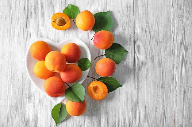 Plate in shape of heart with fresh apricots on wooden background