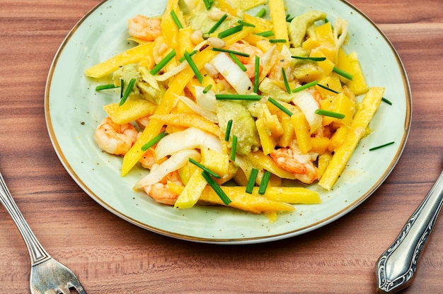 A plate of shrimp stir fry with a fork and spoon on a wooden table.