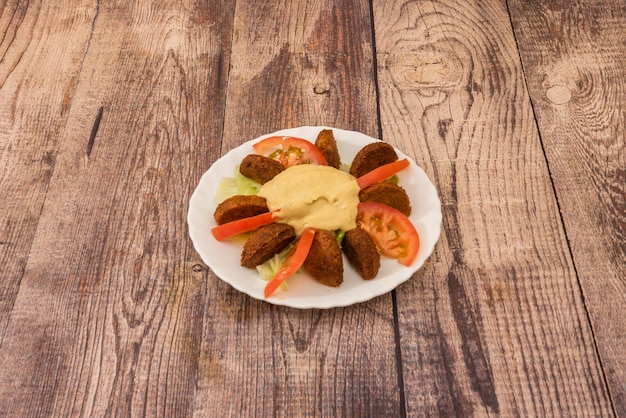 Тарелка нарезанного фалафеля и хумуса с нарезанными помидорами и листьями салата