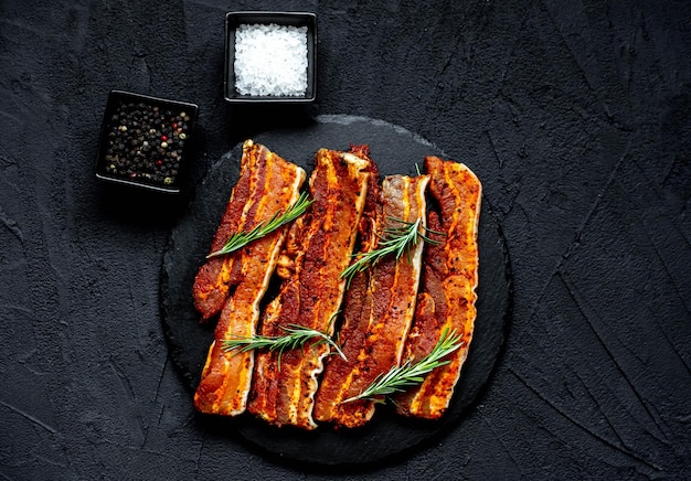 A plate of smoked ribs with salt and pepper on a black background.