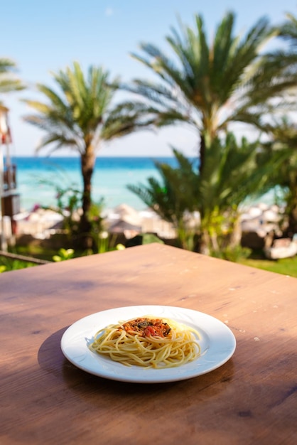 Тарелка спагетти на столе в ресторане с видом на море Еда в отпуске, время расслабиться