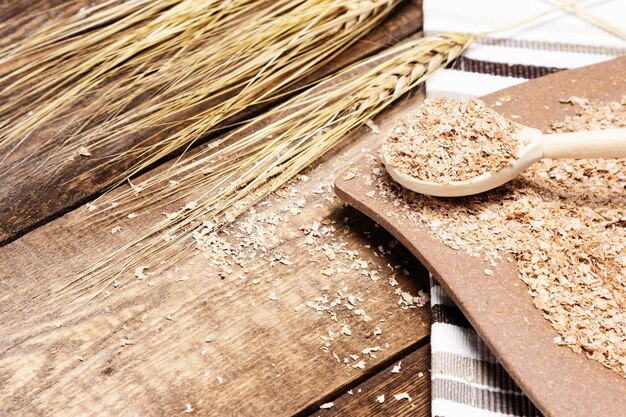 Plate and spoon filled wheat bran next to wheat ears on wood table Healthy eating concept