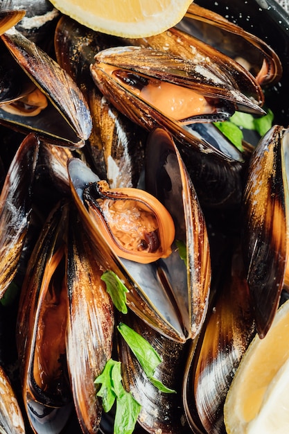 Plate of steamed mussels with lemon and parsley on a rustic wooden table.