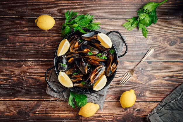 Plate of steamed mussels with lemon and parsley on a rustic wooden table.