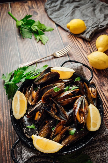 Plate of steamed mussels with lemon and parsley on a rustic wooden table.