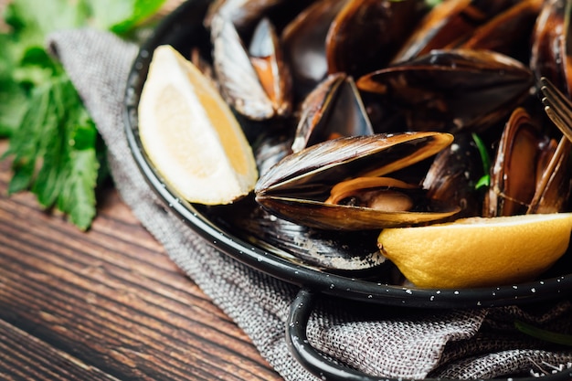 Plate of steamed mussels with lemon and parsley on a rustic wooden table.