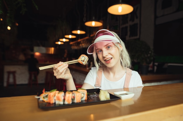 Plate of sushi rolls in restaurant with woman holding chopsticks