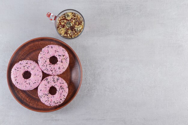 Plate of sweet pink donuts with cup of hot tea on stone table. 