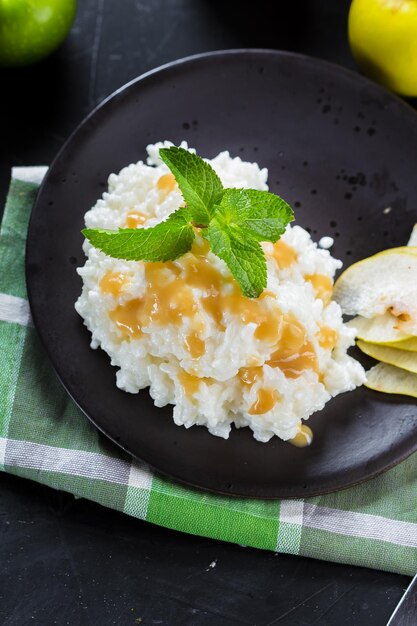 Foto su un piatto porridge di riso dolce con sciroppo di pera, pomodorini, posate su un nero isolato