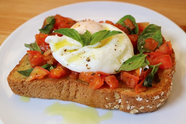 Piatto di pomodoro fresco gustoso e sano e pane tostato al basilico condito con uovo in camicia